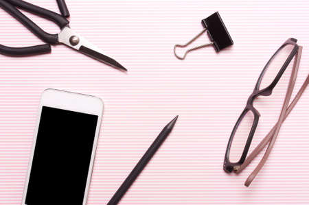 Pencil, glasses, phone, pen, scissors on a pink striped background. Work place. View from above, flatの写真素材