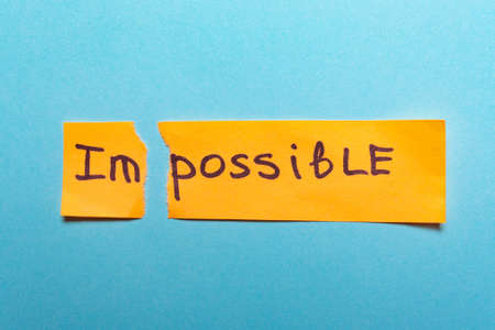The word impossible is written on yellow paper and torn on a blue background.success and challenge concept,motivation, achievement, goalの写真素材