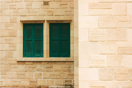 Green shutters on the old wall, made of stone in a row