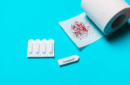 suppository and toilet paper on a blue background, for the treatment of hemorrhoids