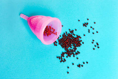 pink menstrual cup  with a drop of blood on a blue background. Concept of women's health, hygienic means of protection, menstruation, ecology of the planet.の写真素材