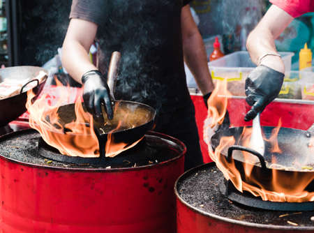 Cooking food in pans at a street festival, fire with red barrels.の写真素材