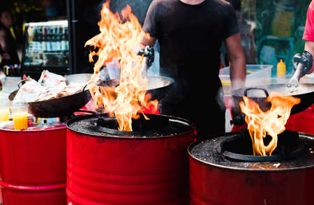 Cooking food in pans at a street festival, fire with red barrels.