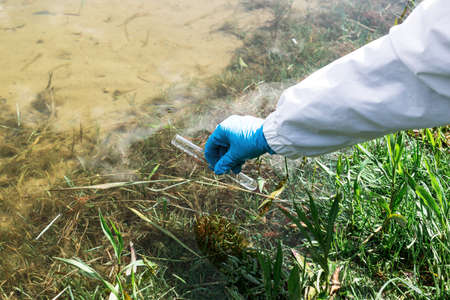 Fence, check the water sample for infections. Gloved hand with a flask and a test tube on a...