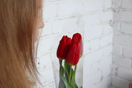 Blonde girl pensively looks at a bouquet of red tulips close upの写真素材