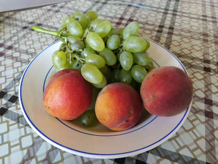 Juicy fruit grapes and peach on a plateの写真素材