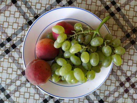 Juicy fruit grapes and peach on a plateの写真素材
