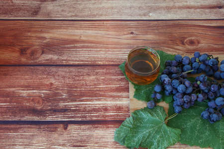 Blue grape bunches with leaves and glass of wine on brown wooden background with copyspaceの写真素材