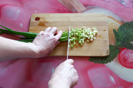 Woman cuts green onions on the cutting board, first person viewの写真素材