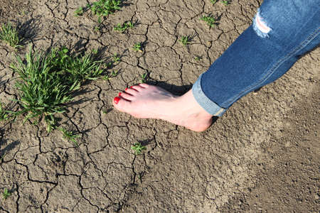 Woman's foot in jeans on a background of cracked ground and grass