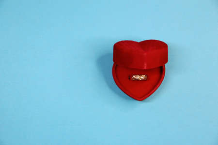 Golden ring the red velvet box in the form of a heart on the blue background, with copy spaceの写真素材