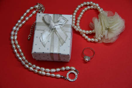 White jewelry box with bow near jewelry on red background, gift with copy spaceの写真素材