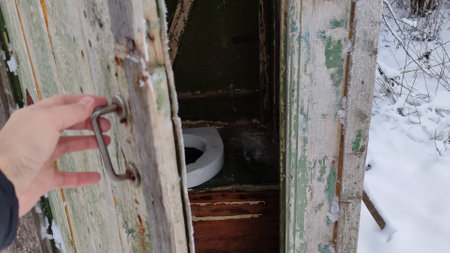 A person in a winter setting closes a door to an old village toilet and leavesの写真素材