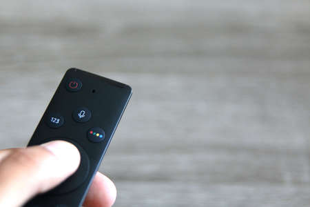 hand pressing remote control over a light grey background