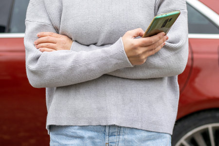 woman in front of lateral door red car in warm pullover blue jeansの写真素材