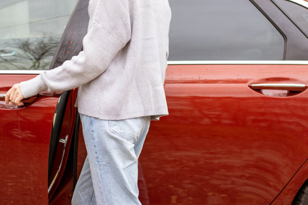 woman in front of lateral door red car in warm pullover blue jeans