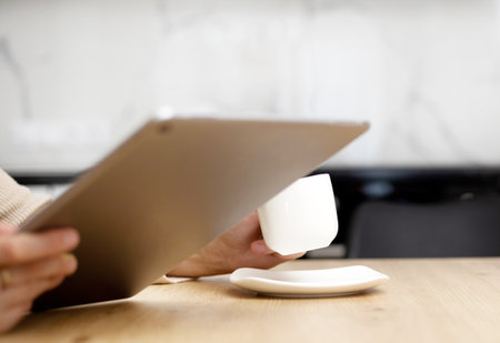 woman drinking coffee and using tablet pad sitting at kitchenの写真素材