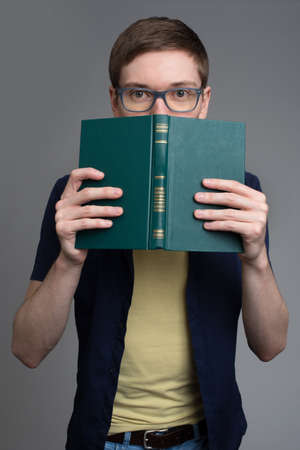 Surprised young man in glasses looking out of the bookの写真素材