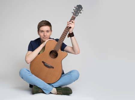 Portrait of a young man sitting with guitar against gray background
