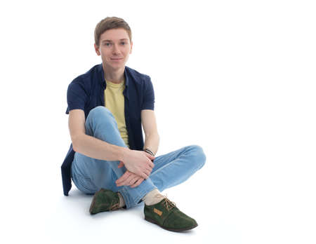 Pensive stylish young man sitting on floor isolated on white backgroundの写真素材