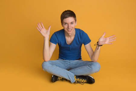 A young guy sitting on the floor isolated on orange backgroundの写真素材