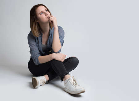 Portrait of a smiling young girl sitting on the floor isolated on a white backgroundの写真素材