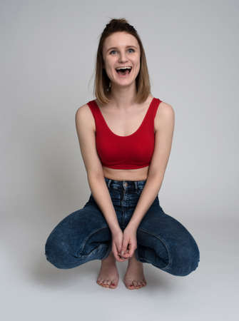 Portrait of a casual happy woman sitting on the floor on gray backgroundの写真素材