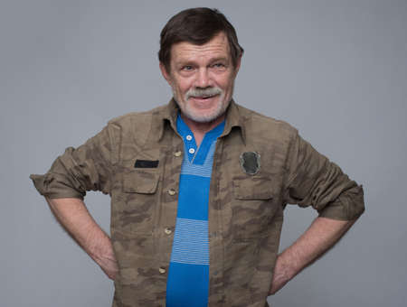 Studio shot of senior man standing with his hands on hips laughing against grey backgroundの写真素材