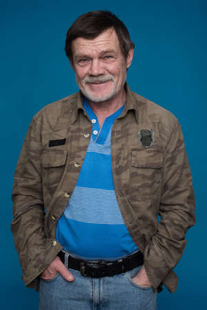 an elderly man with a beard, a mustache, holding hands in pockets isolated on a blue backgroundの写真素材