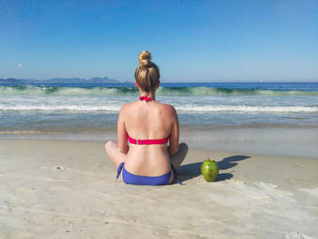 Woman in bikini on the beach sitting next to a coconut - Copacabana, Rio de Janeiro, Brazilの写真素材