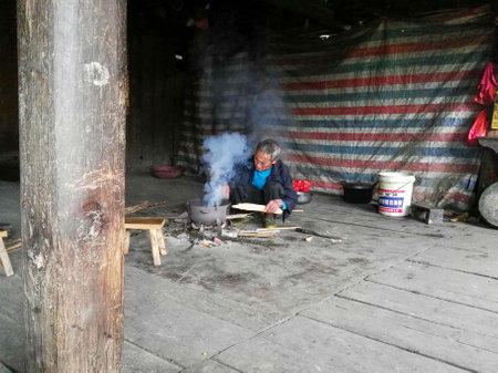 Longsheng, China - November 12, 2016: Man preparing meal on the floor in a pot on fire in wooden houseのeditorial素材
