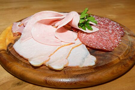 cold cuts with a sprig of parsley on a wooden round boardの写真素材