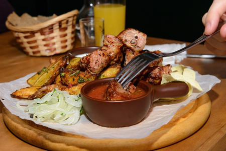 Hand with a fork dips a piece of meat in the sauceの写真素材