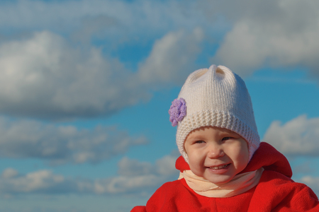 baby in warm clothes laughs against the sky with cloudsの写真素材