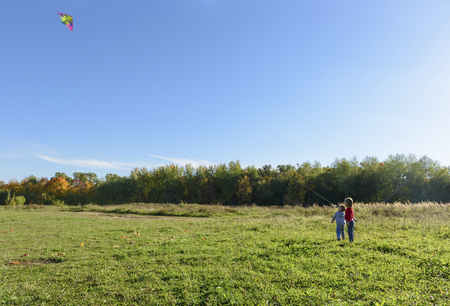 Children run the kite in the meadow in the autumn forestの写真素材