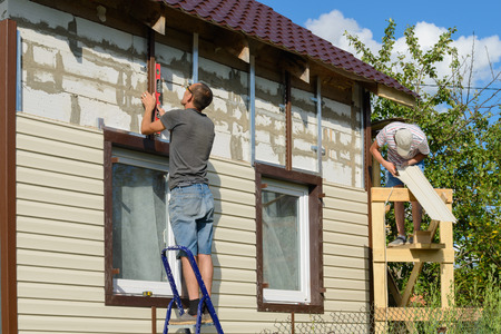 August 6, 2017: Photo of two workers cover the facade of the building with vinyl siding. Cheboksary. Russia.のeditorial素材