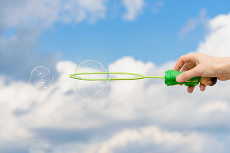 hand with a toy launches soap bubbles against the sky
