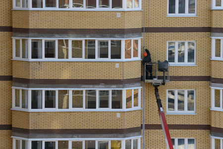 worker on an autotower repairs the facade of an apartment brick residential buildingの写真素材