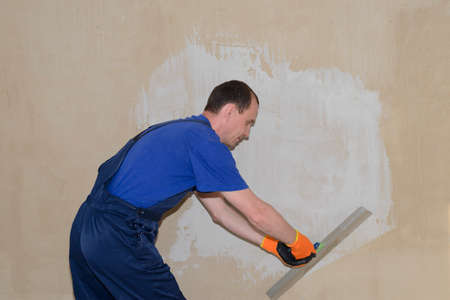 A plasterer in overalls puts white putty on the wallの写真素材