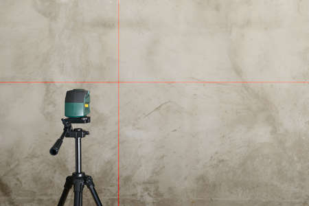 The laser level stands on a tripod and projects its beams onto a gray wall
