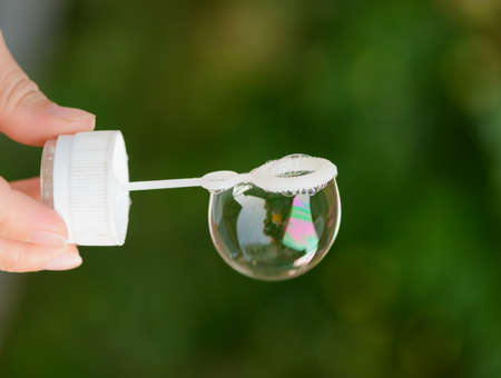The hand holds a stick with a soap bubble on a green background