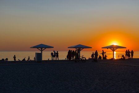 beach with umbrellas and silhouettes of people at sunsetの写真素材