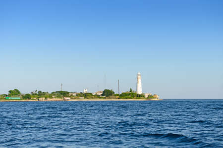 The sea shore with buildings and a white lighthouse on a sunny summer dayの写真素材