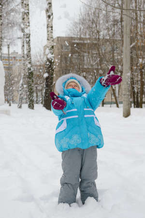 A little girl in a blue winter jacket plays with snowの写真素材