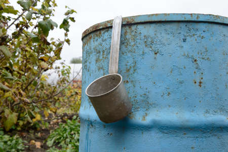 An aluminum bucket hangs on a metal blue barrel in the autumn gardenの写真素材