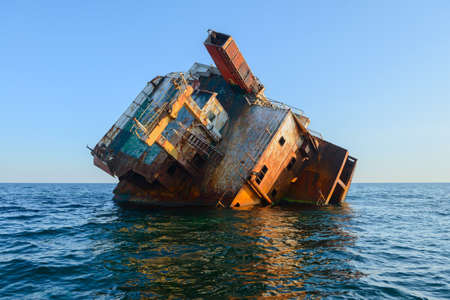The rusty frame of a stranded naval ship in the middle of the seaの写真素材