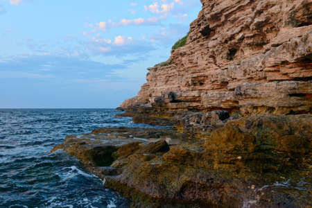 Steep rocky seashore with waves at sunsetの写真素材