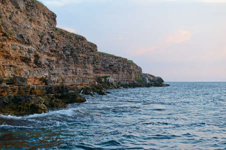 Steep rocky seashore with waves at sunsetの写真素材