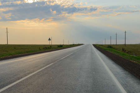 An asphalt road in the middle of a field with the rays of the sun through the cloudsの写真素材