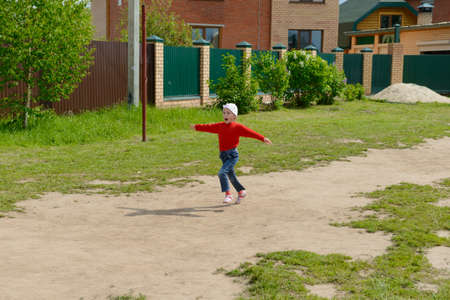 A smiling child in red clothes runs with his arms outstretched in the courtyard of a private houseの写真素材